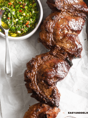 close up of grilled picanha steak in a skewer with a side of chimichurri sauce on a table.