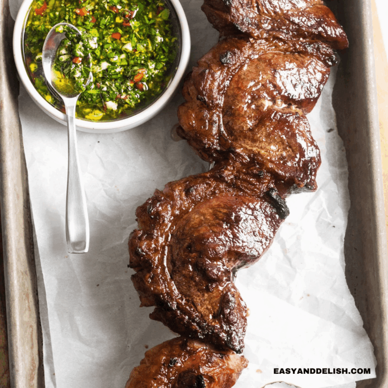 close up of grilled picanha steak in a skewer with a side of chimichurri sauce on a table.
