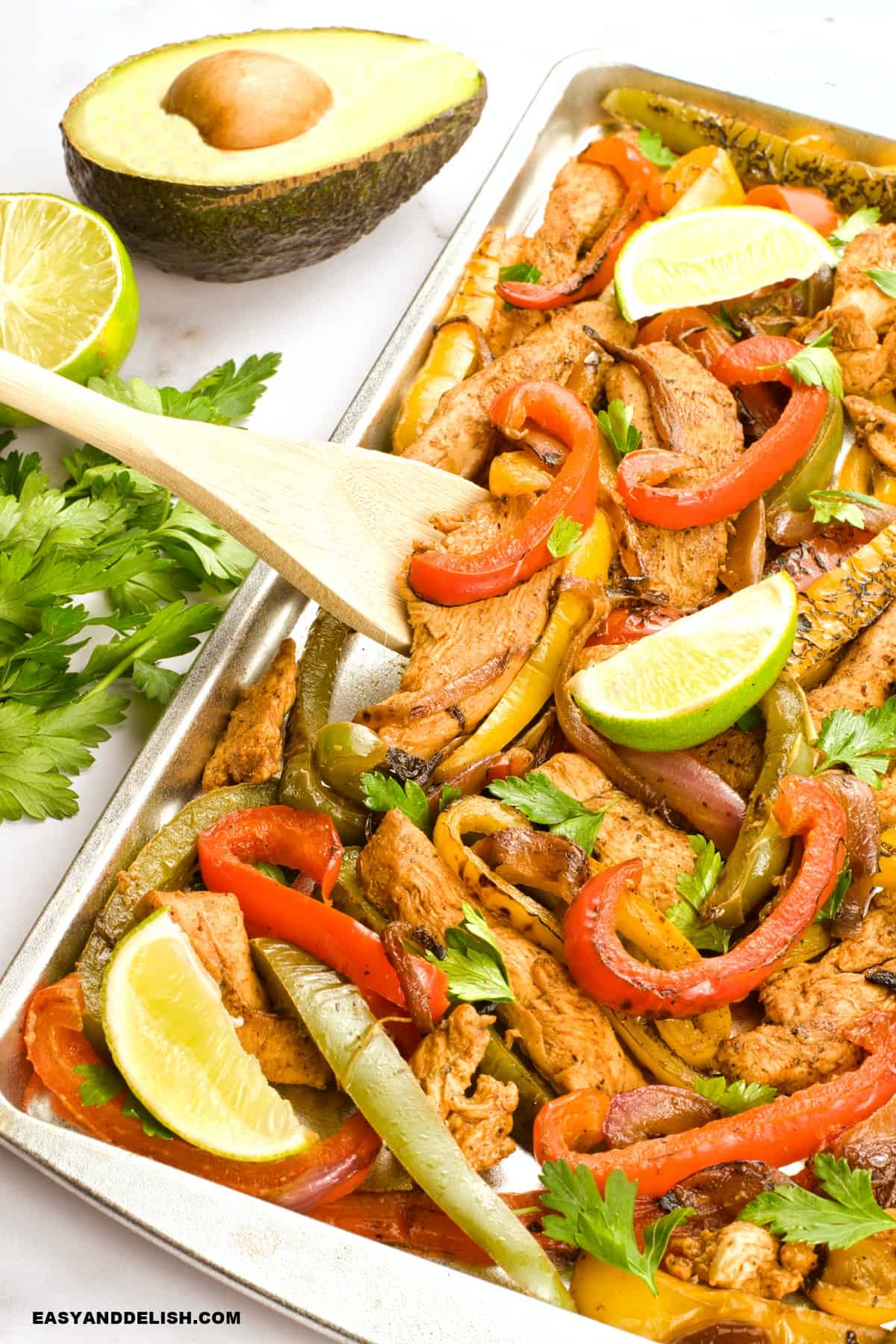 a spoon removing a portion of keto chicken fajitas ina  sheet pan. 