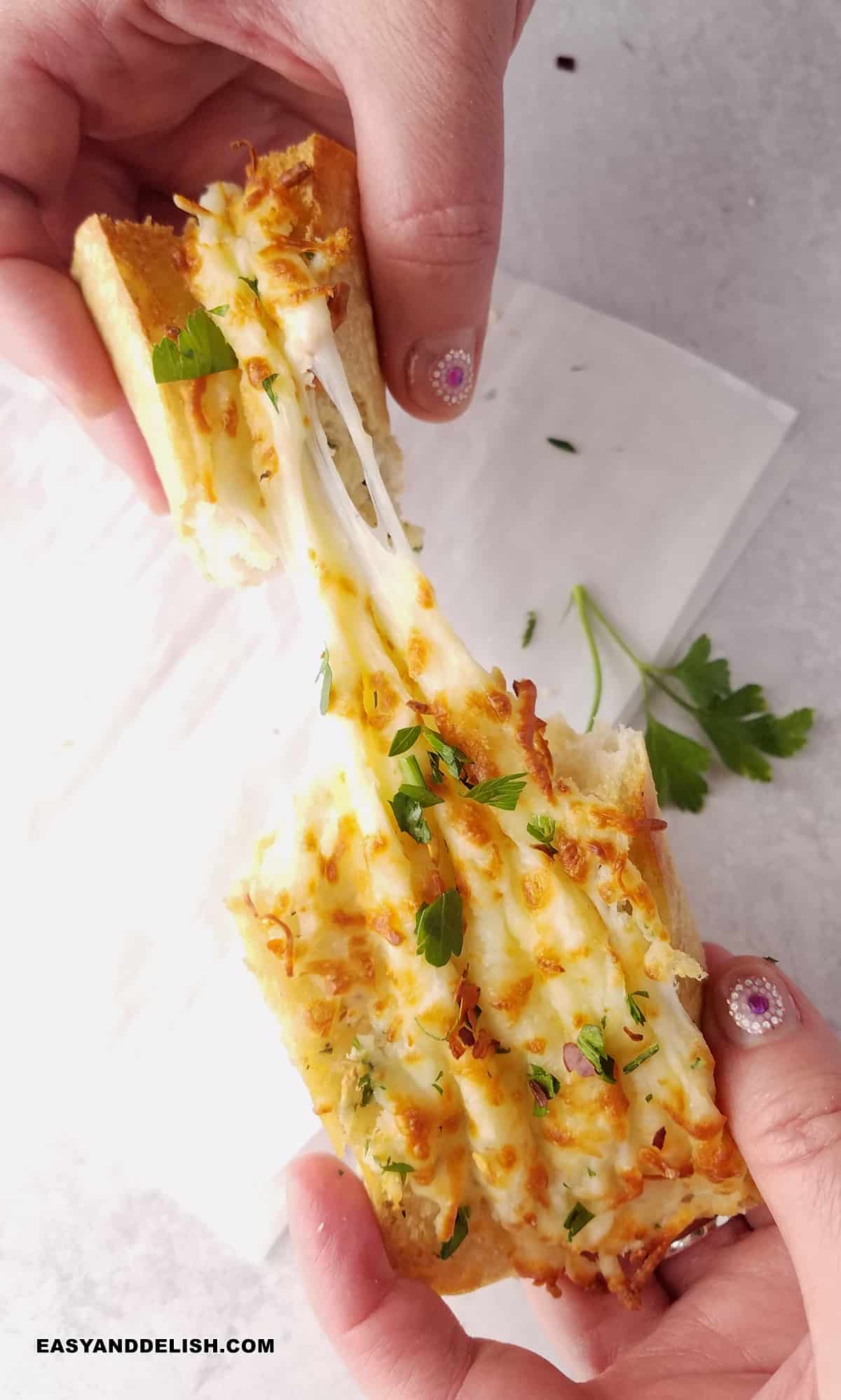 a hand pulling the melting cheesy top of a slice of air fryer garlic bread.