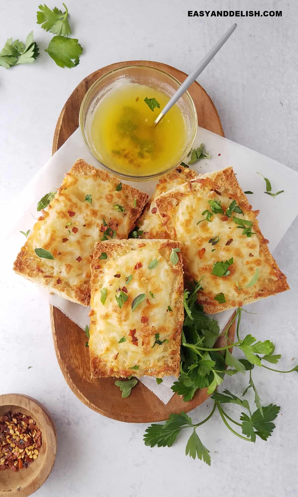 a tray full of slices of baked cheesy baguette with butter on the side and fresh parsley..