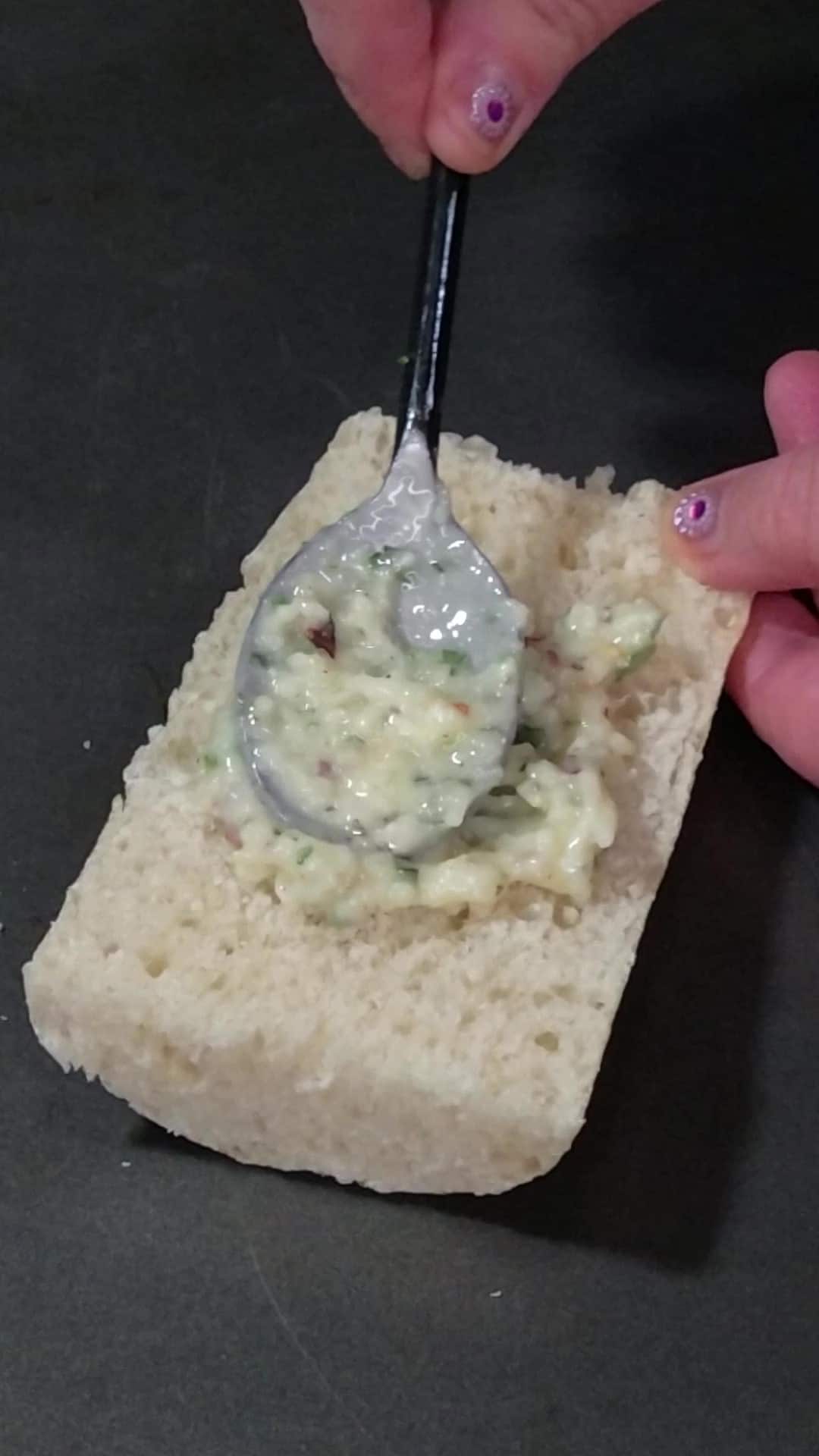 spreading garlic bread spread onto a slice of baguette.