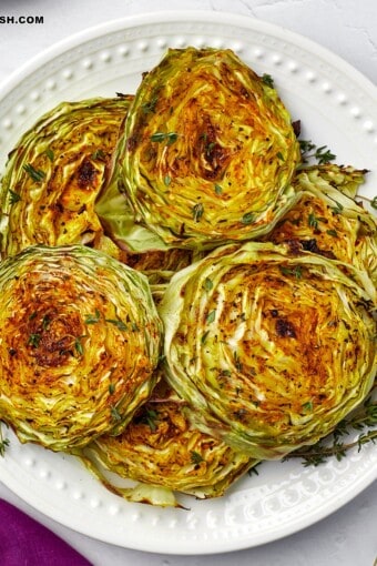 a close up of a plate full of cabbage steaks topped with fresh herbs.