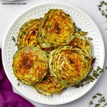 a close up of a plate full of cabbage steaks topped with fresh herbs.