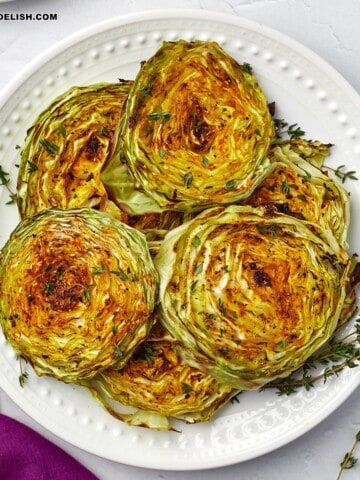 a close up of a plate full of cabbage steaks topped with fresh herbs.