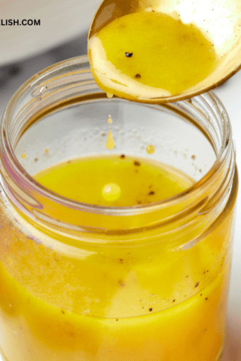 close up of a jar with maple dijon vinaigrette and a spoon pouring the dressing into it.