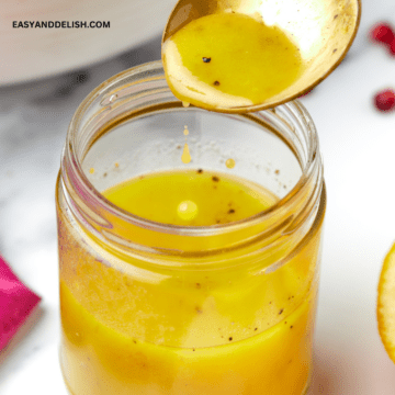 close up of a jar with maple dijon vinaigrette and a spoon pouring the dressing into it.