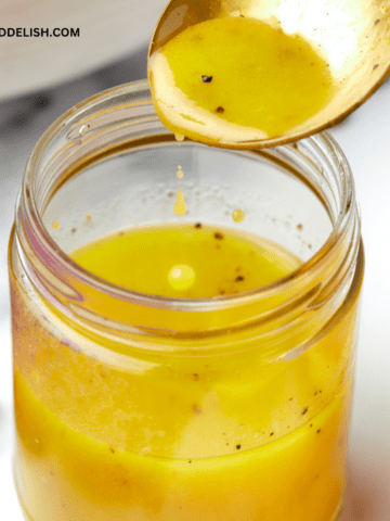 close up of a jar with maple dijon vinaigrette and a spoon pouring the dressing into it.