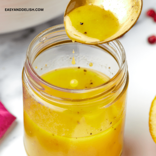 close up of a jar with maple dijon vinaigrette and a spoon pouring the dressing into it.
