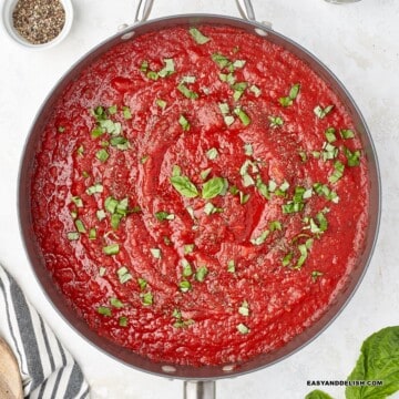 close up of a pan with healthy hearty marinara sauce and fresh herbs with some ingredients on the side.