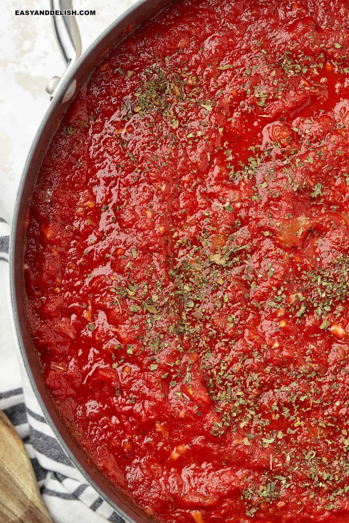 Marinara sauce with dried basil and oregano in a skillet.