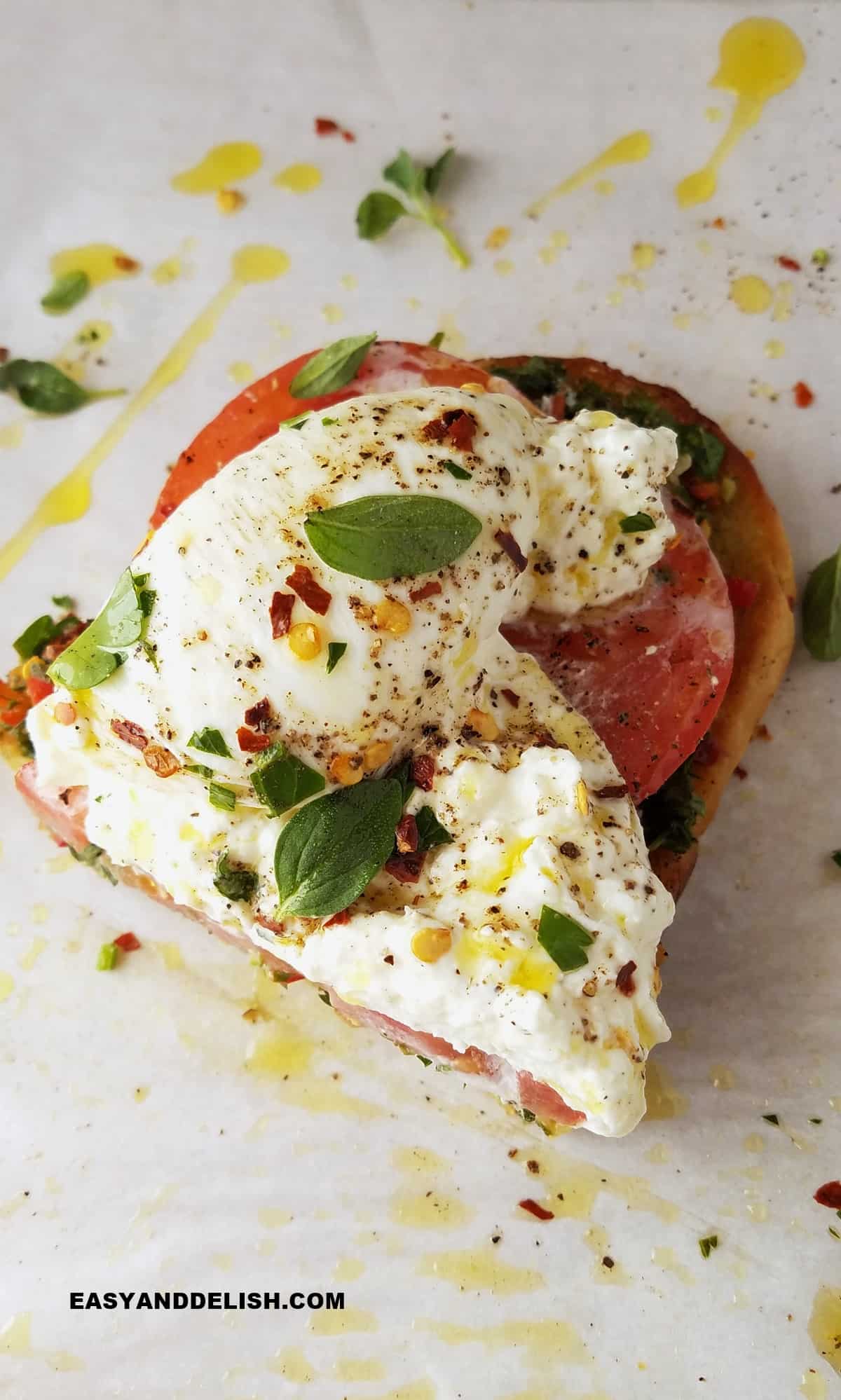 half of a tomato burrata toast drizzled with EVOO and topped with fresh herbs.