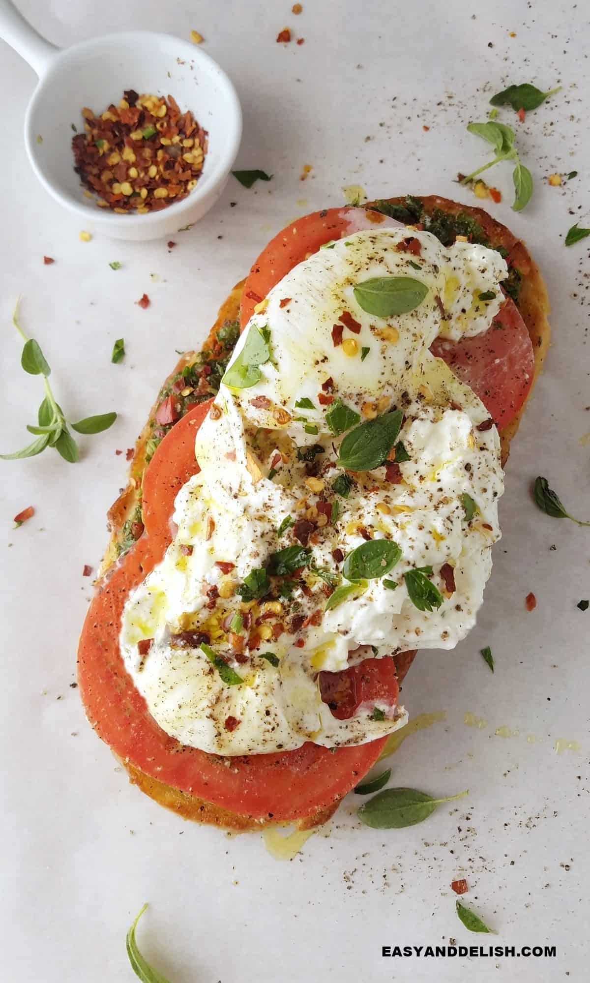 a slice of burrata toast with a small bowl of red pepper flakes on the side.