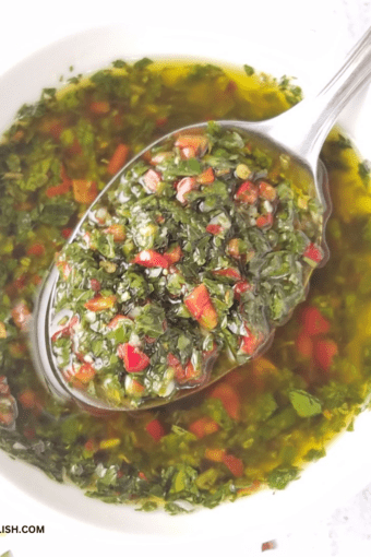 close up of a bowl of authentic chimichurri with a spoon of sauce held over it.