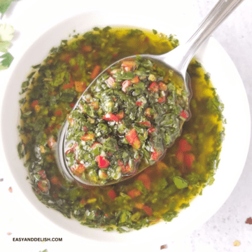 close up of a bowl of authentic chimichurri with a spoon of sauce held over it.