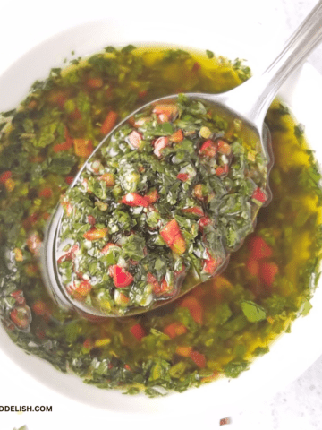 close up of a bowl of authentic chimichurri with a spoon of sauce held over it.