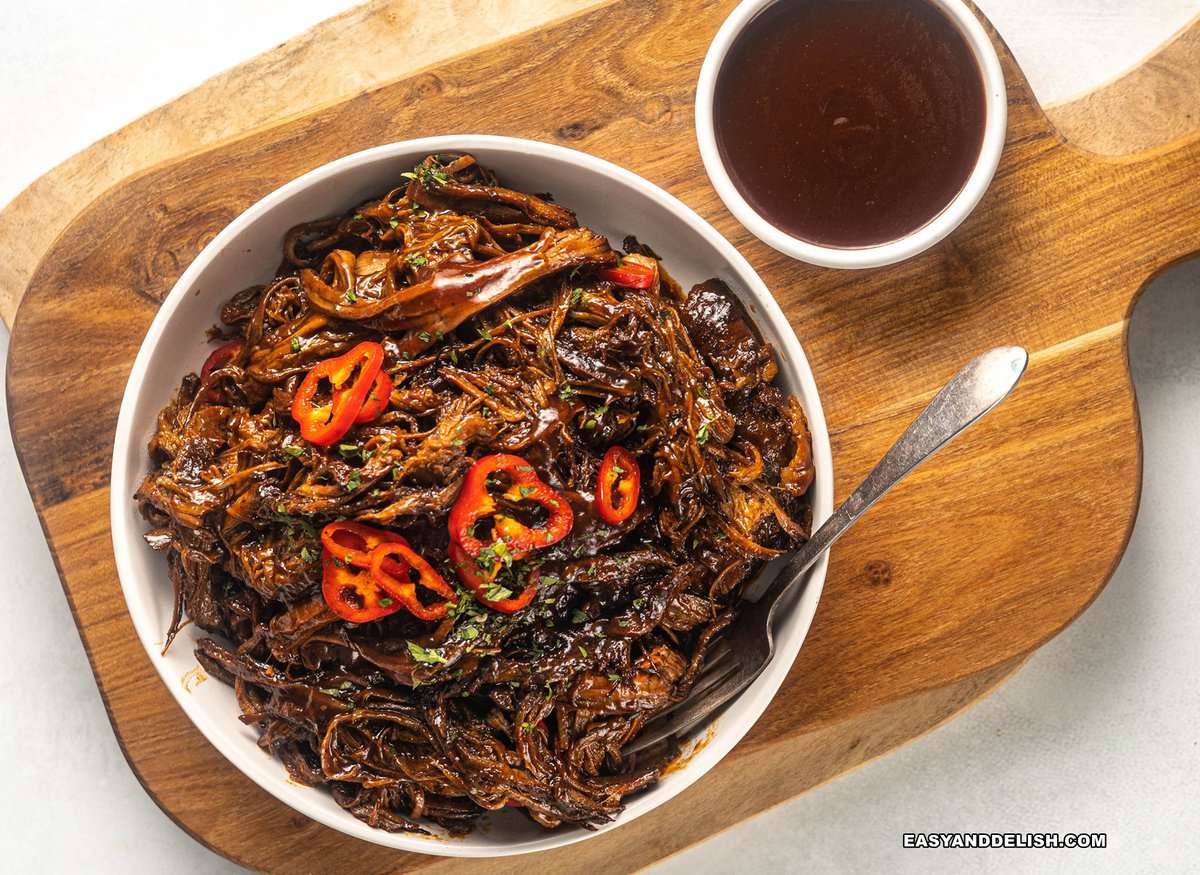 shredded beef in a bowl with a fork on the side and also a small bowl of barbecue sauce nearby.
