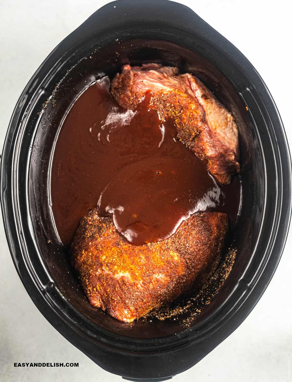 beef with dry rub in a slow cooker partially covered with barbecue sauce.
