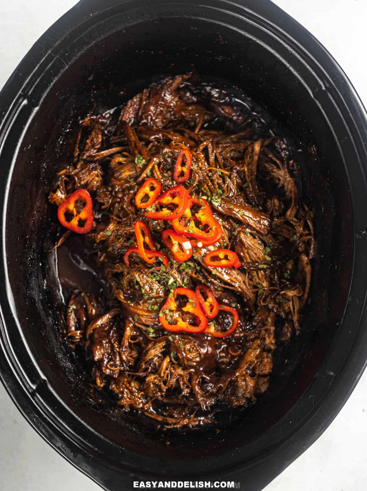 shredded brisket in a slow cooker garnished with hot red peppers.