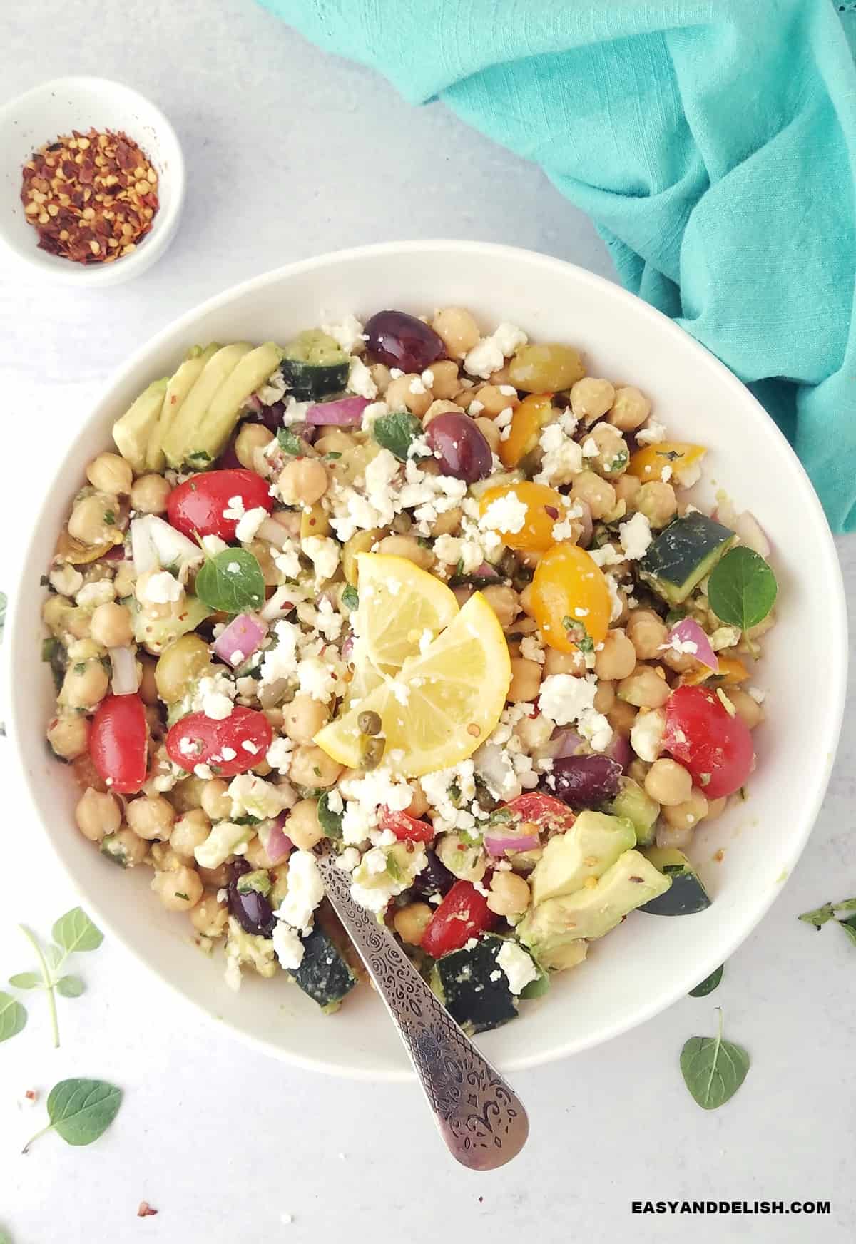 cucumber tomato chickpea salad with avocado in a serving bowl with seasonings on the side. 