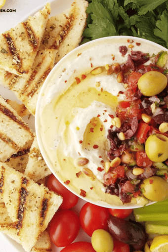 close up of half of a bowl of whipped ricotta dip with grilled toast and crudites on the side.