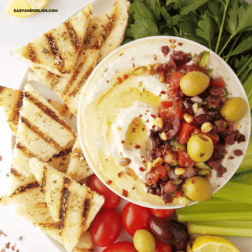 close up of half of a bowl of whipped ricotta dip with grilled toast and crudites on the side.
