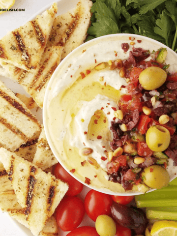 close up of half of a bowl of whipped ricotta dip with grilled toast and crudites on the side.