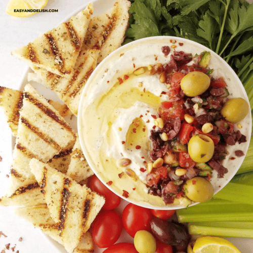 close up of half of a bowl of whipped ricotta dip with grilled toast and crudites on the side.