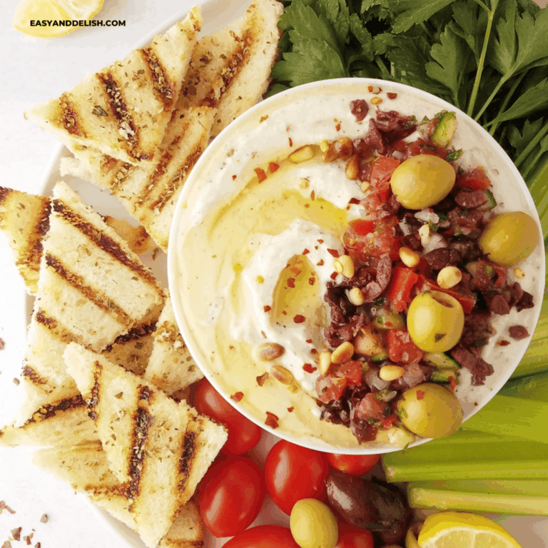 close up of half of a bowl of whipped ricotta dip with grilled toast and crudites on the side.