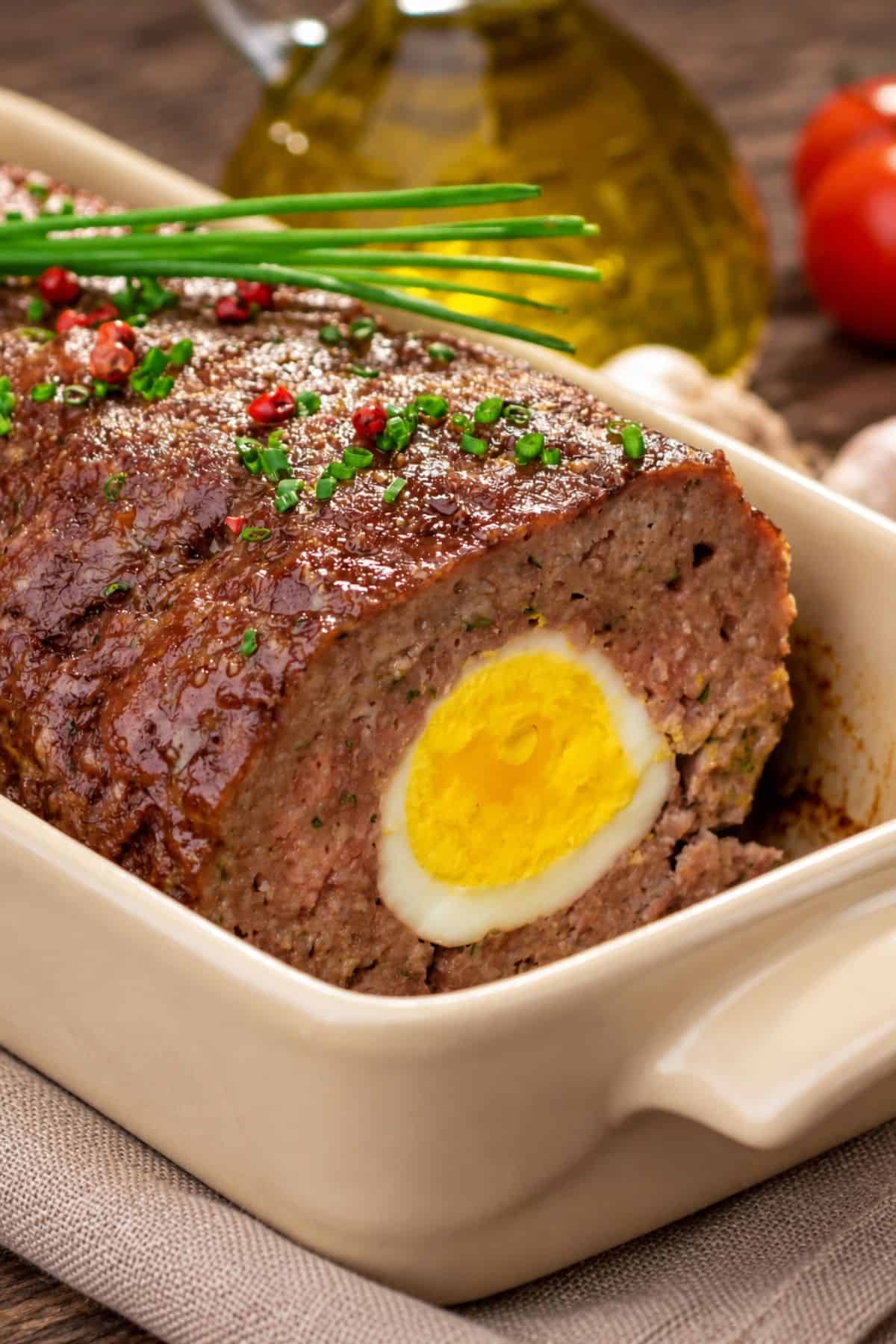 Close-up of a browned beef loaf with a hard-boiled egg center and chopped chives on top.