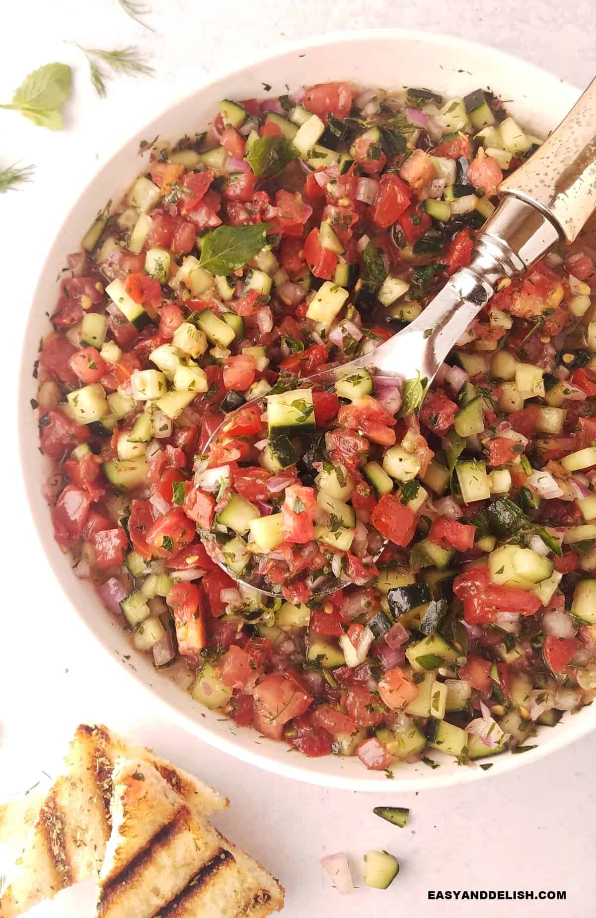 a spoon grabbing some Persian cucumber salad with some toasts on the side. 