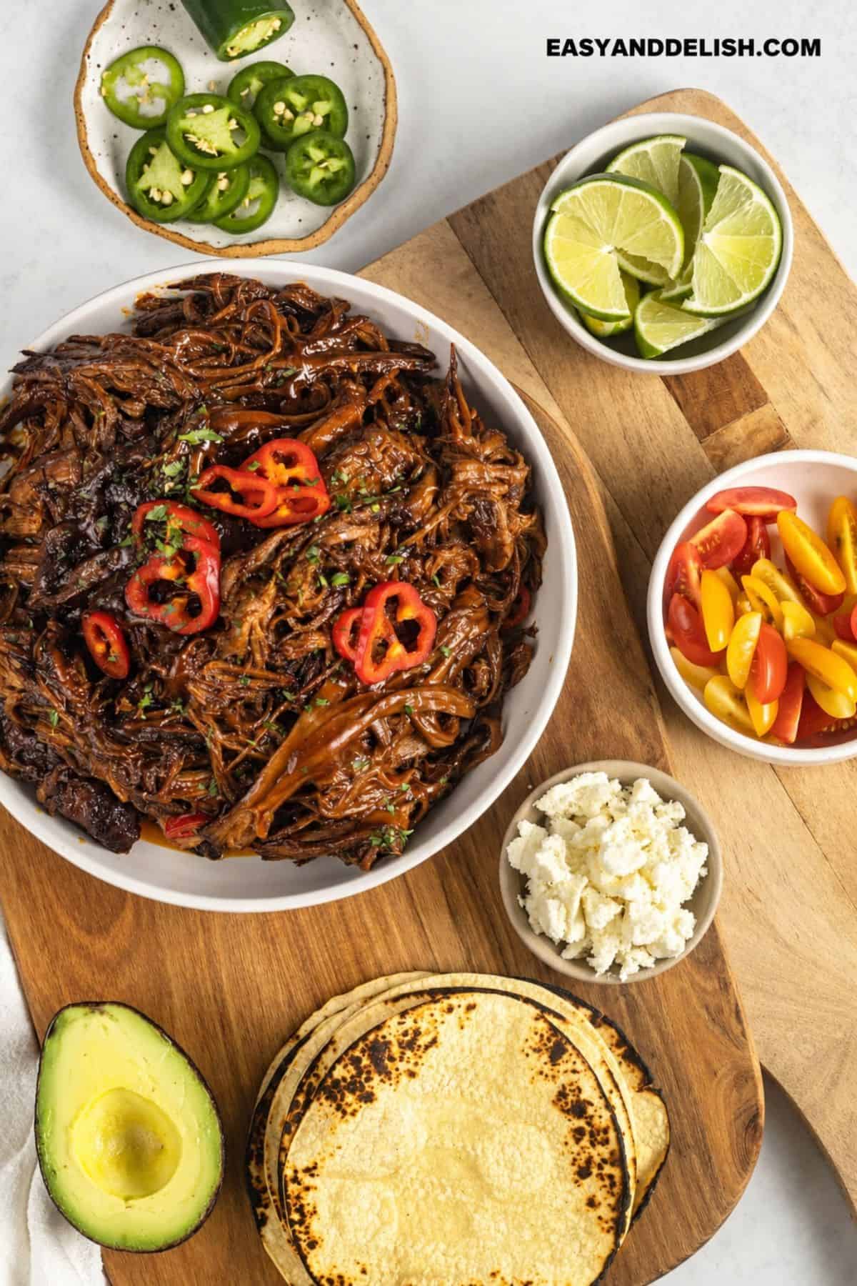 Shredded brisket served with tortillas, avocado, lime, peppers, cheese, and tomatoes.
