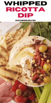 close up of whipped ricotta dip in abowl with a piece of toasted dipped in it.