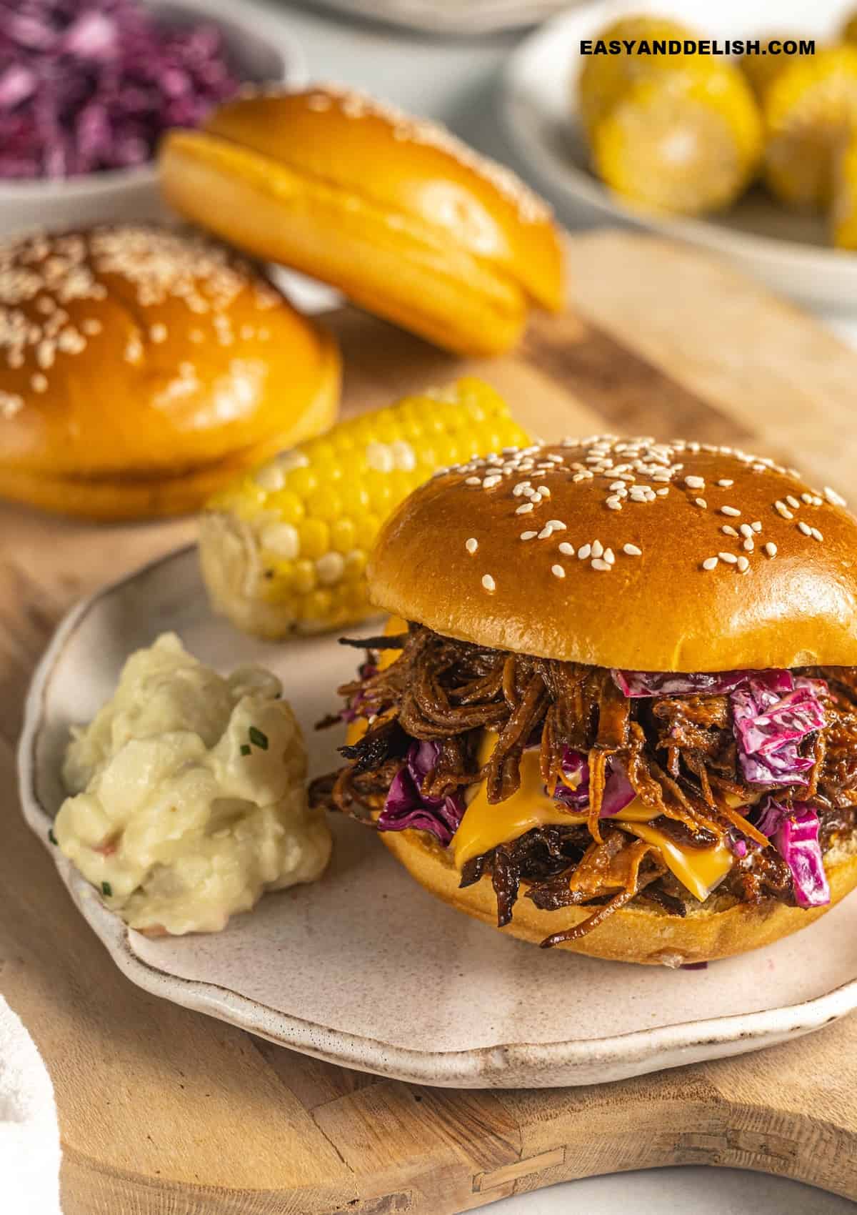 bbq beef brisket sandwich with potato salad and corn on the cob served on a table. 