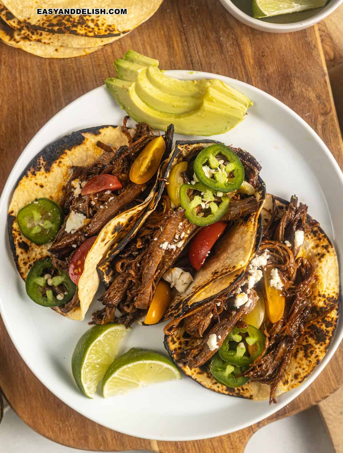 three shredded beef tacos garnished on top and with avocado slices on the side. 