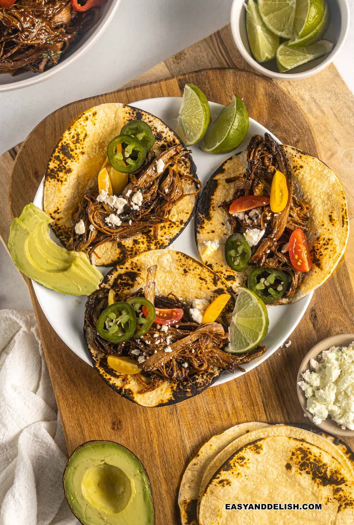 three crockpot brisket tacos with garnishes around them. 