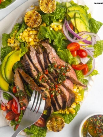 A forkful of flank steak salad taken from a platter.