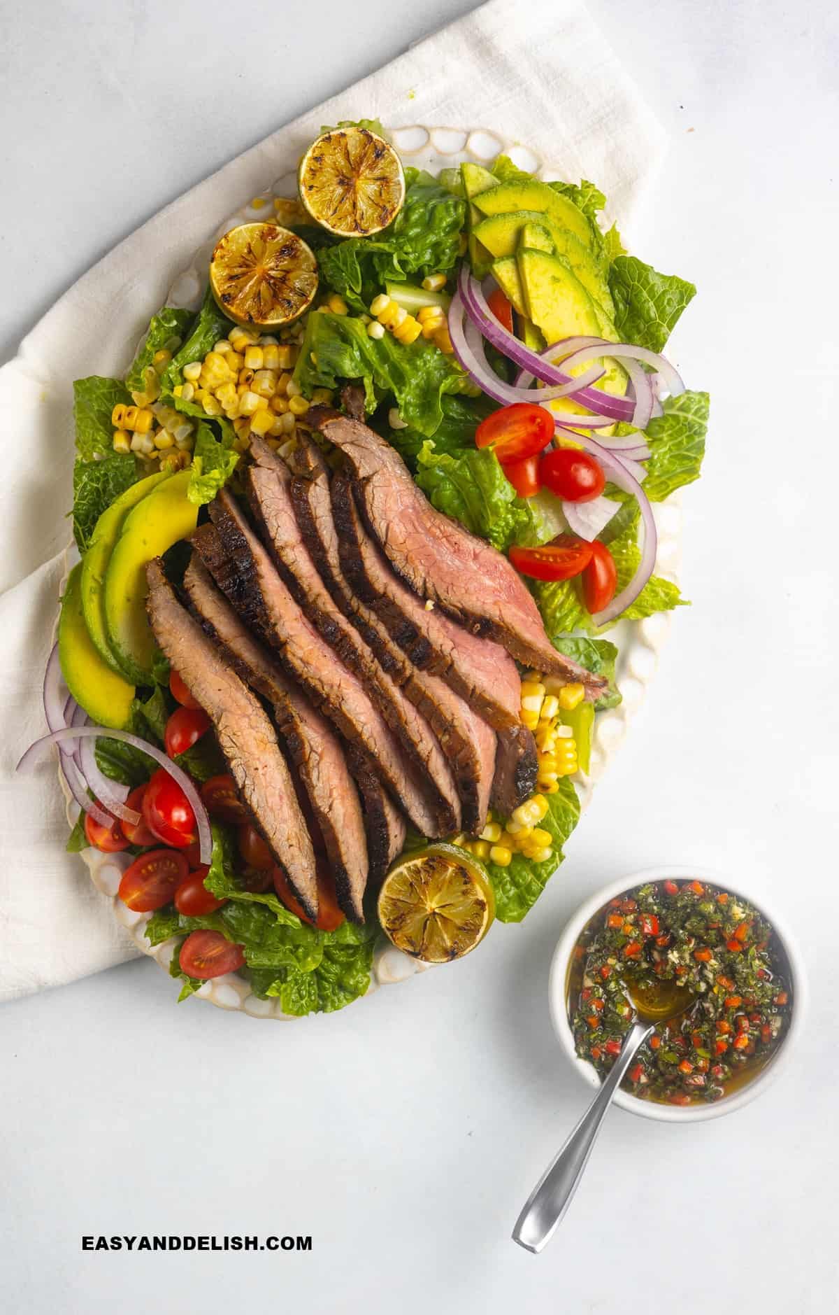 steak salad ina  platter with a bowl of chimichurri dressing on the