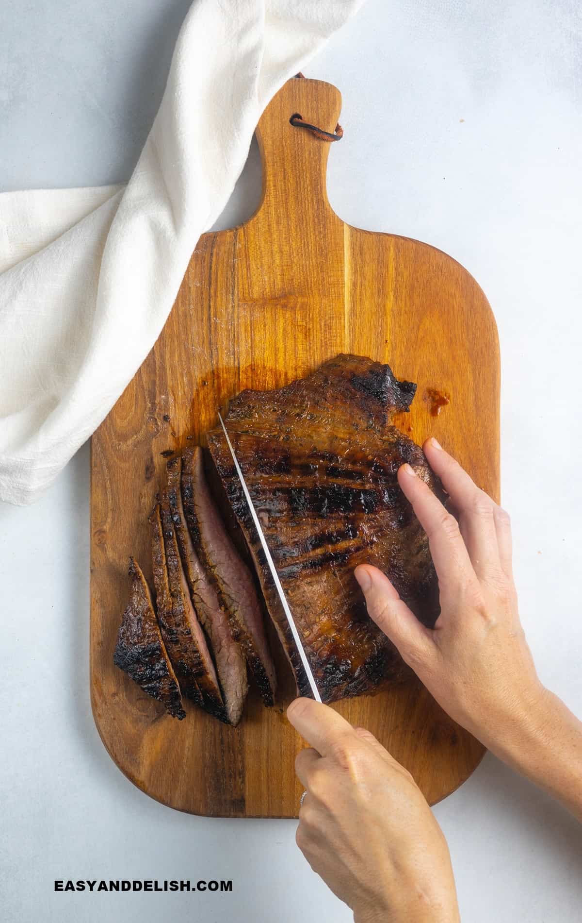 flank steak on a cutting board being sliced against the grain.