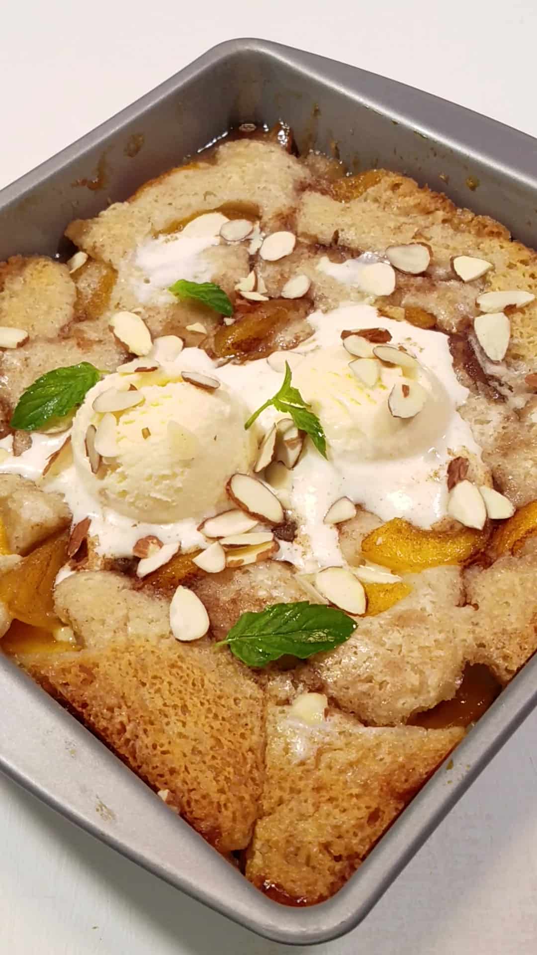 baking pan with lazy man peach cobbler, scoops of ice cream, mint leaves, and toasted almonds.