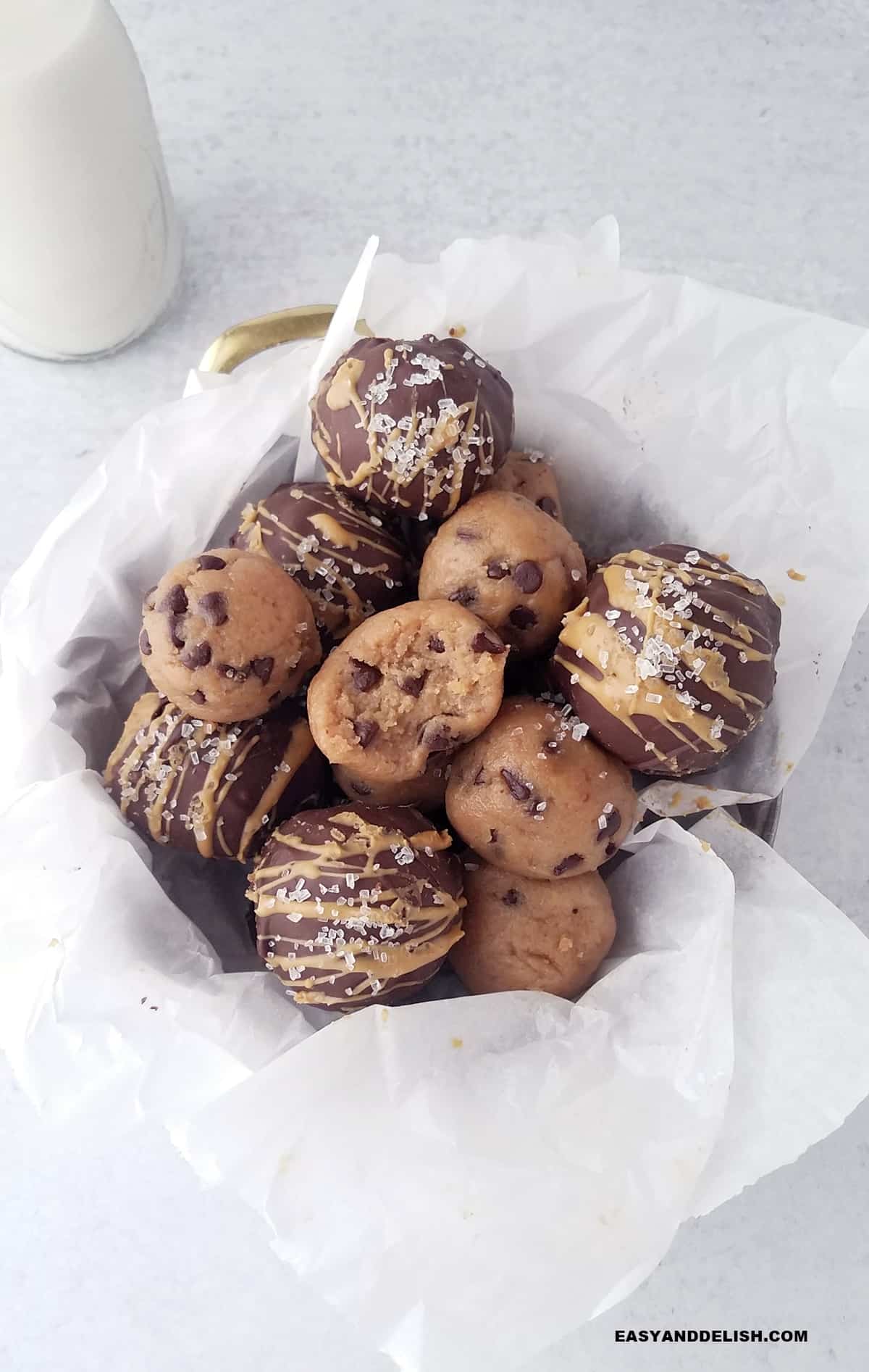 a pile of cookie dough protein bites in a basket with a bottle of milk on the side.