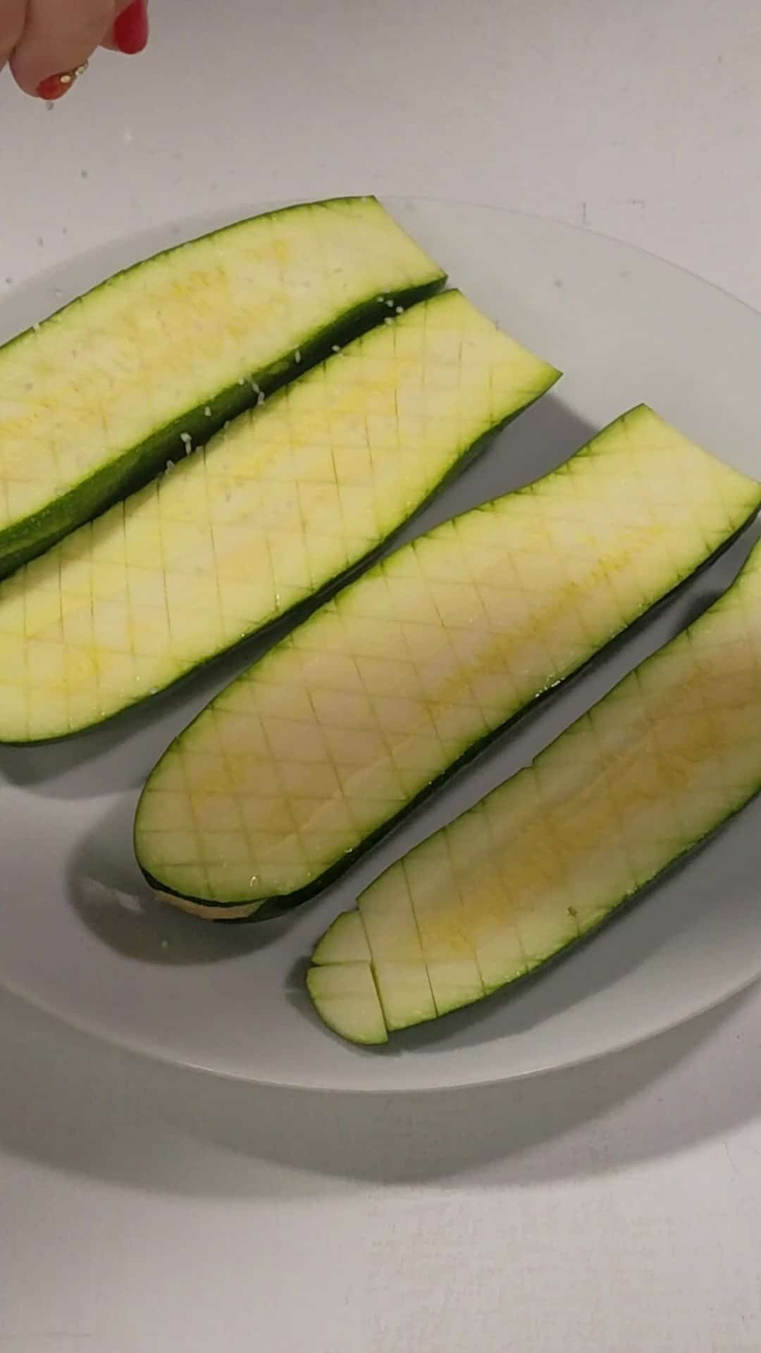 Scored and salted zucchini halves in a plate.