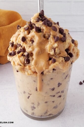 a glass with protein cookie dough with chocolate chips and a drizzle of peanut butter.