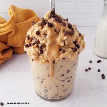 a glass with protein cookie dough with chocolate chips and a drizzle of peanut butter.