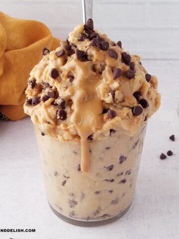 a glass with protein cookie dough with chocolate chips and a drizzle of peanut butter.