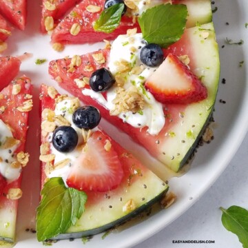 close up image of some slices of watermelon pizza topped with yogurt, berries, granola, honey, chia, and mint.
