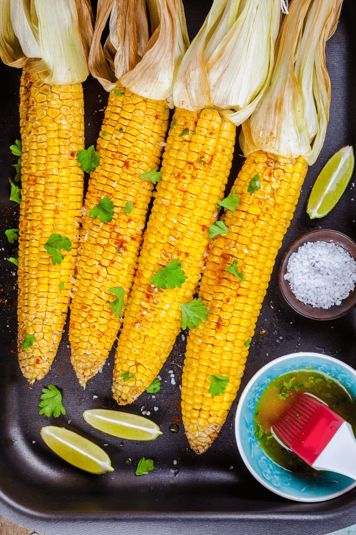 four ears of the summer vegetable in a platter with garnishes on top and around them.