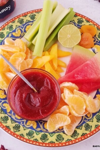 a bowl with homemade chamoy sauce served ina platter with assoreted fruits.