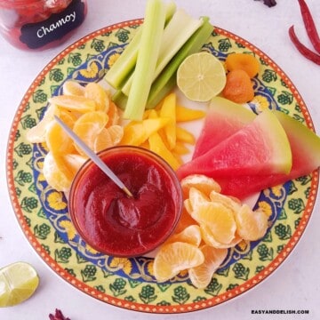 a bowl with homemade chamoy sauce served ina platter with assoreted fruits.