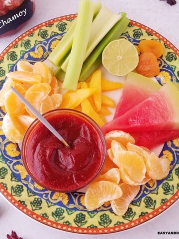 a bowl with homemade chamoy sauce served ina platter with assoreted fruits.